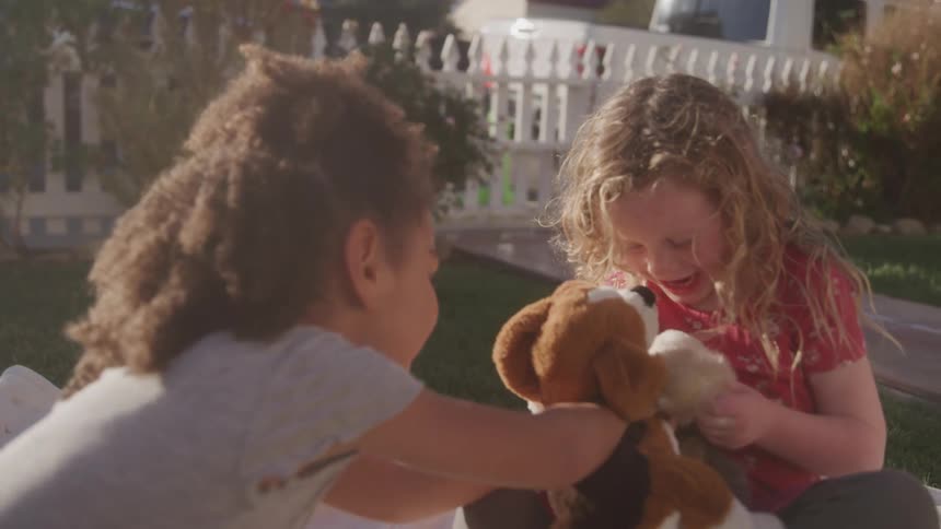Two little girls playing in the yard with teddy bears