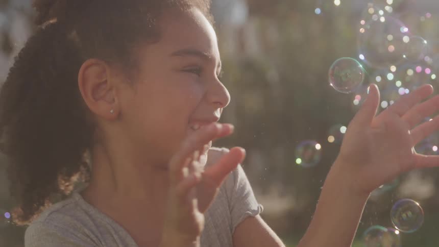 Little girl with curly hair playing with soap bubbles in a backyard