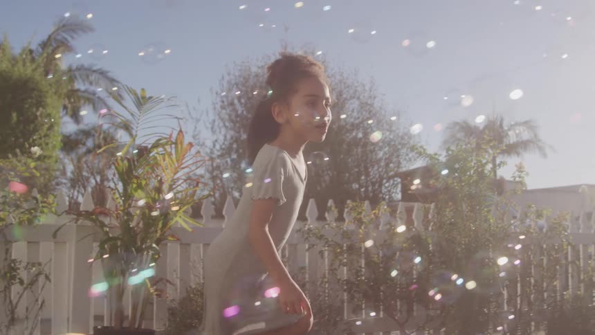 Joyful young girl plays in backyard with floating bubbles