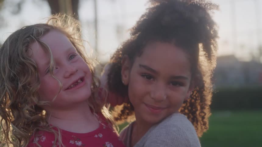Two young girls hug and smile in sunset light
