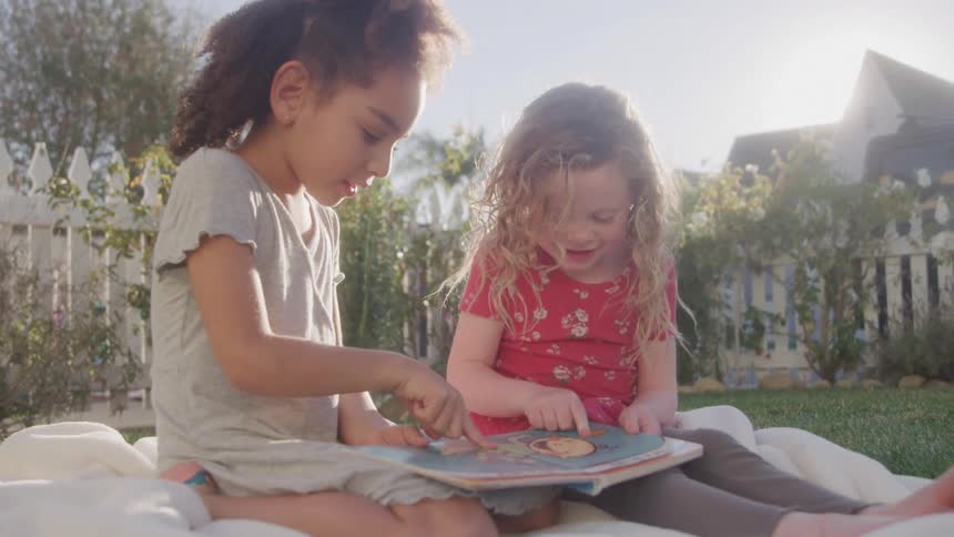 Two children looking at books in a backyard