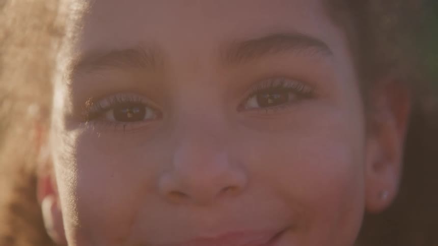A young childs face fills the frame with a warm sunlit smile and expressive eyes