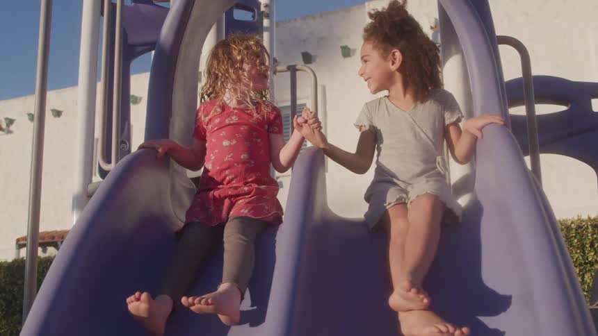 Two young girls play joyfully on a slide in sunlight