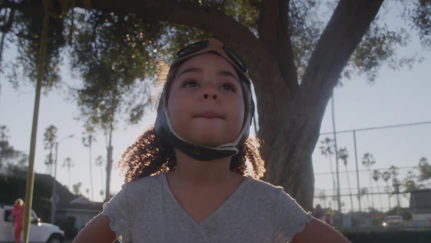 A young girl wears aviator goggles and looks up confidently