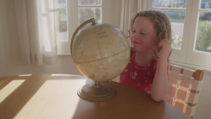 Little girl sitting at a table and interacting with the globe