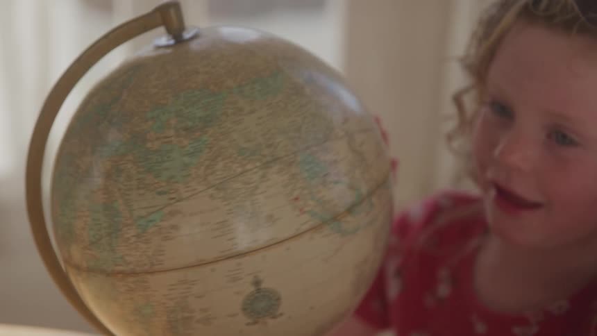 A young child gazes at a spinning globe with curiosity and delight