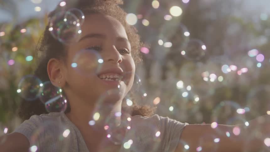 Joyful girl plays with soap bubbles in warm sunlight
