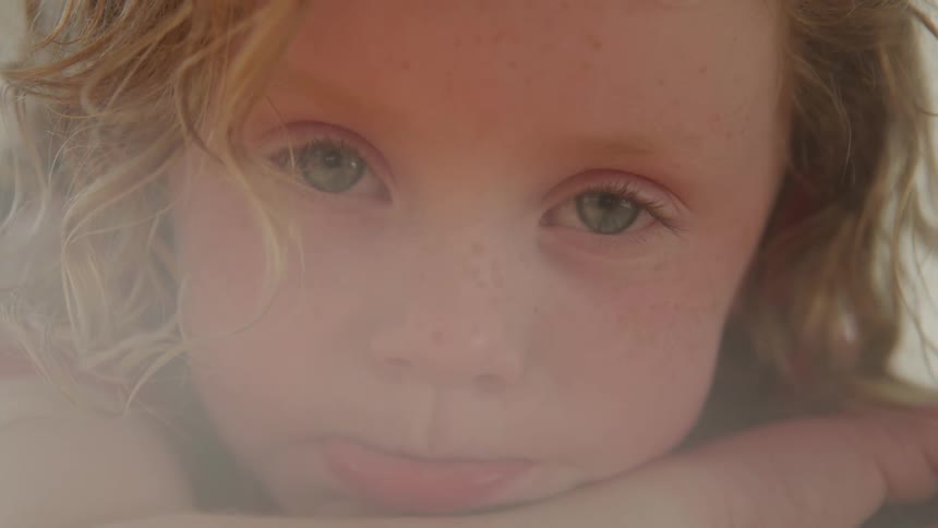 A closeup shot of a young child with fair skin and freckles initially shown with eyes closed their eyes then open to reveal bright blue or green irises as they look directly at the camera