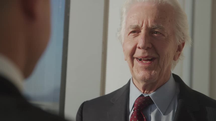 Close up of a young office worker conversing with an elderly businessman in an office building during daytime