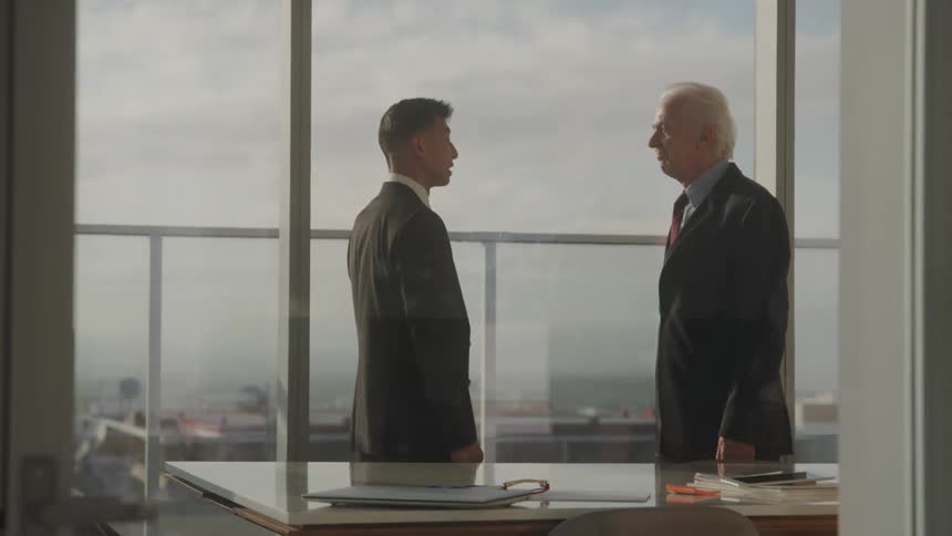 Two businessmen talk seriously by a window in a high rise office