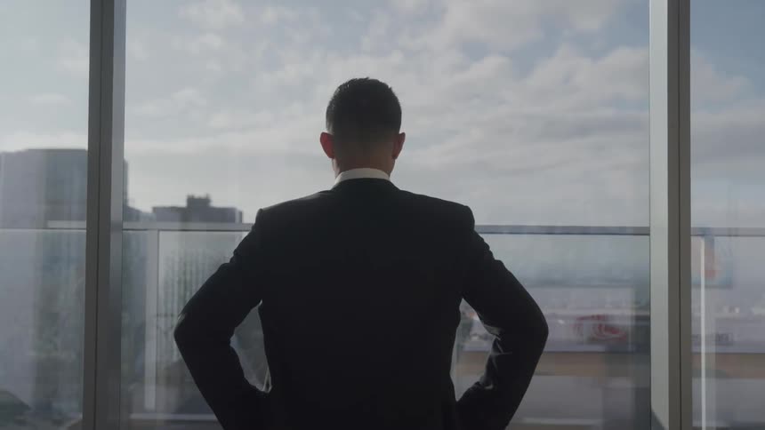 Man in a suit looks out at the city through a glass window
