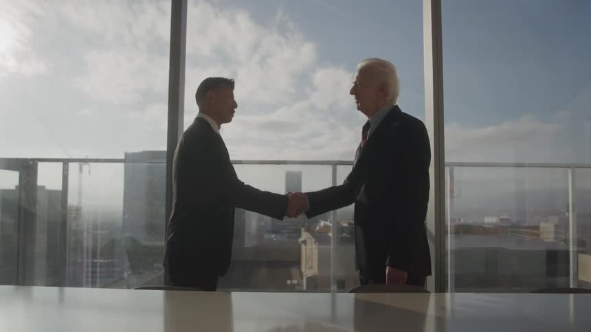 Two men in suits shaking hands in a panoramic office