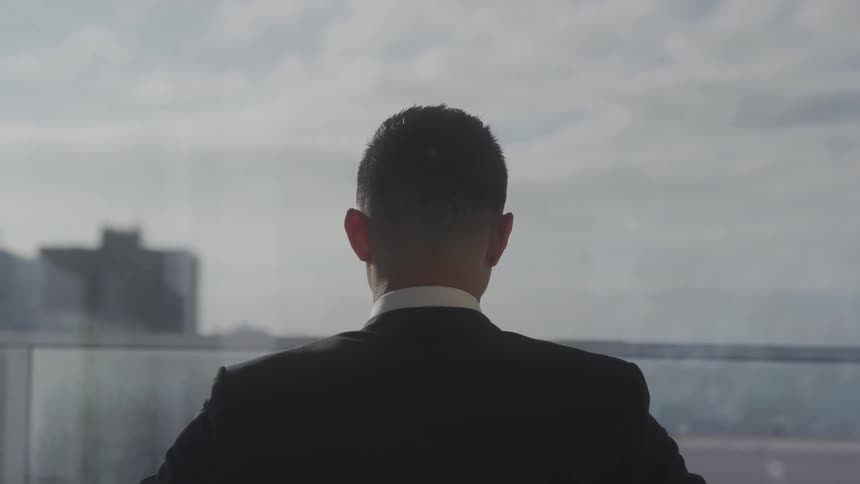 Close up of a young businessman looking through a window in an office building during daytime