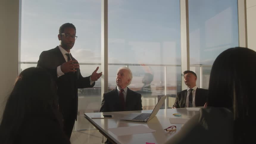 A man stands and speaks to a group of people sitting at the table