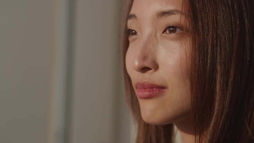 The video shows a closeup of a womans face seen from the side she has dark hair and is looking upwards and slightly to the right with a thoughtful or pensive expression