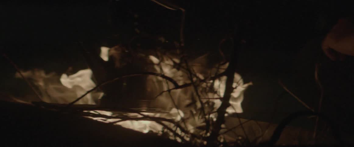 A camp fire heats a kettle at night