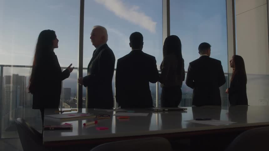 A group of coworkers discuss with each other while standing in a meeting room during daytime