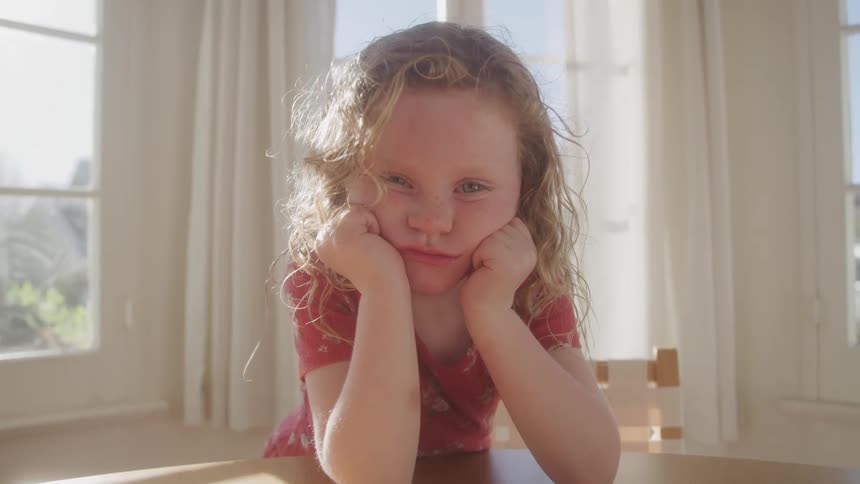 A young girl missing her front tooth places both hands on her cheeks and smiles anyway