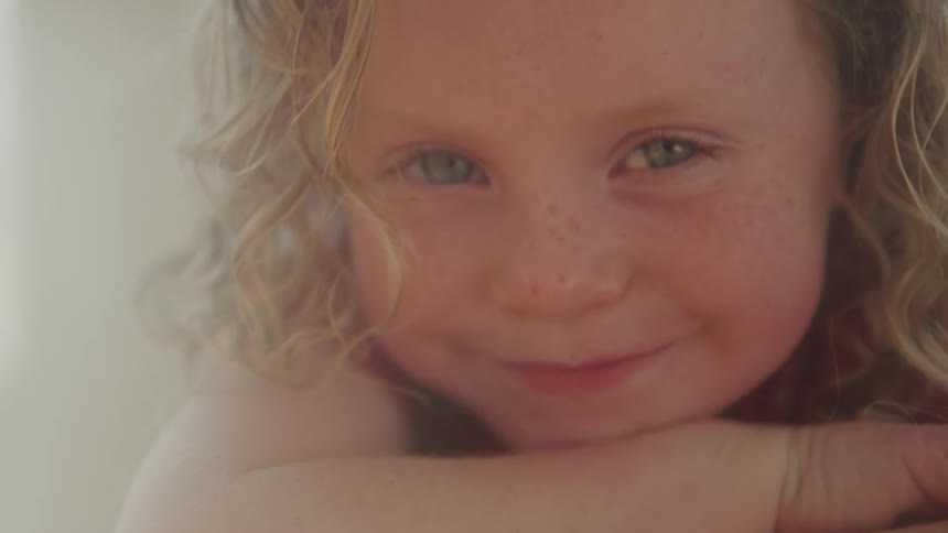 Curly haired girl smiles chin resting on arms