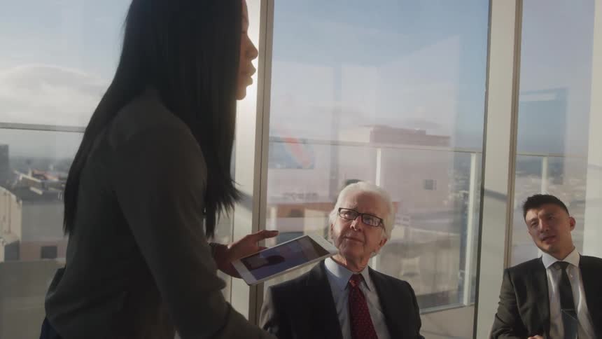 Woman with a tablet talking to two men sitting at an office table
