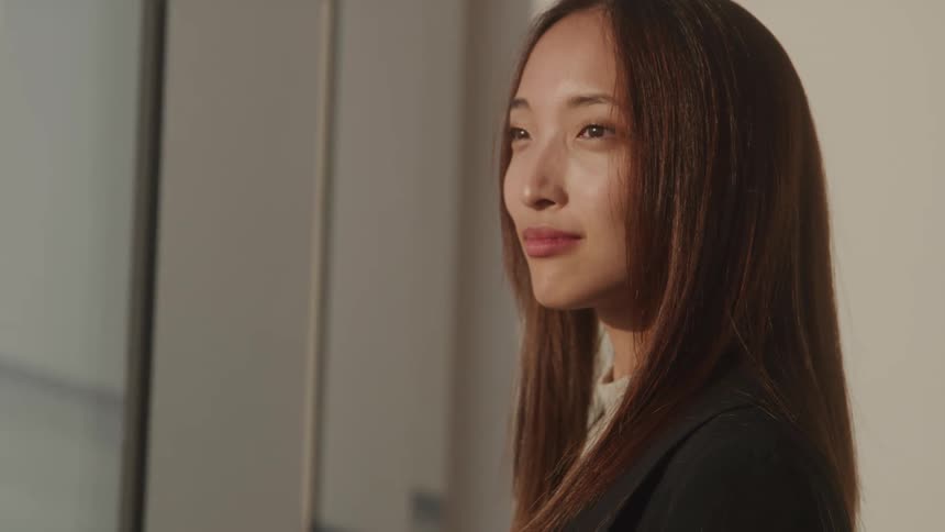 A medium closeup shot of a woman with long straight dark hair is shown she is looking slightly to her right with a gentle expressionthe lighting suggests she might be near a window or an indoor light source