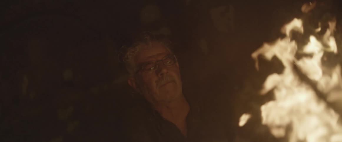A man sits in front of a burning campfire