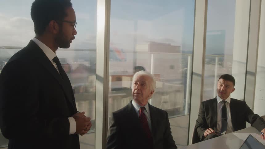 A boss addresses two colleagues during a meeting in a high rise office