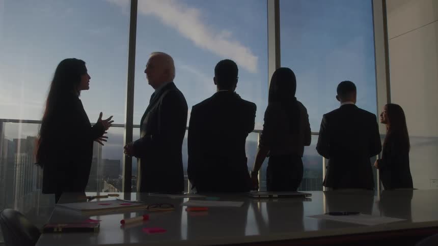 Silhouetted professionals mingle by a high rise window at sunset