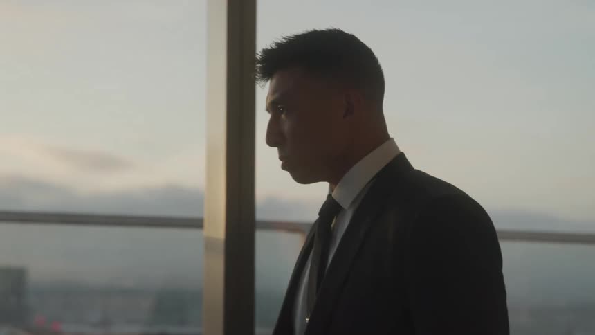 The video shows a man in a suit and tie seen in profile looking out of a large window with a city view in the hazy background he appears thoughtful or contemplative a filmsupply watermark is present in the middle of the frame