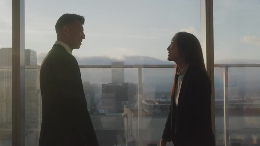 Two professionals shake hands in a high rise office at sunset