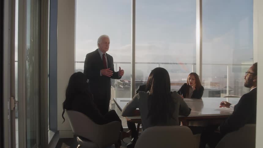 Elderly man in a suit giving a meeting to people sitting at an office table