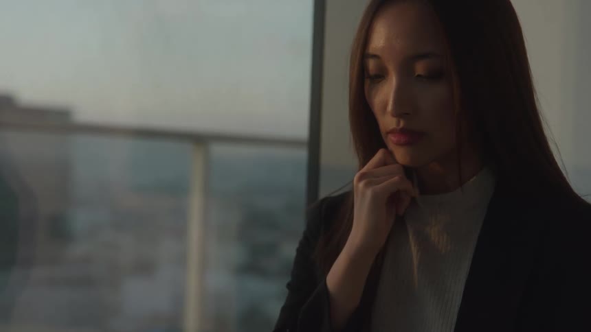A woman stands by a window looking pensive