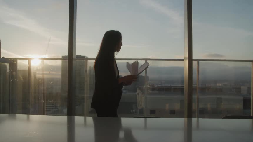 Woman throws papers in front of a window overlooking the city at dusk