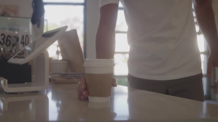 A barista hands coffee to a customer at a cafe counter
