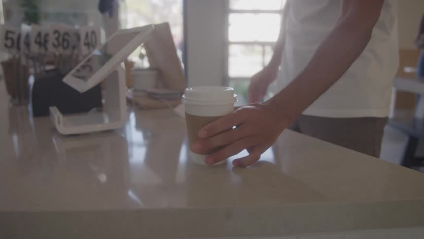 Close up of a female cashier handing a drink over a counter to a male customer in a restaurant during daytime