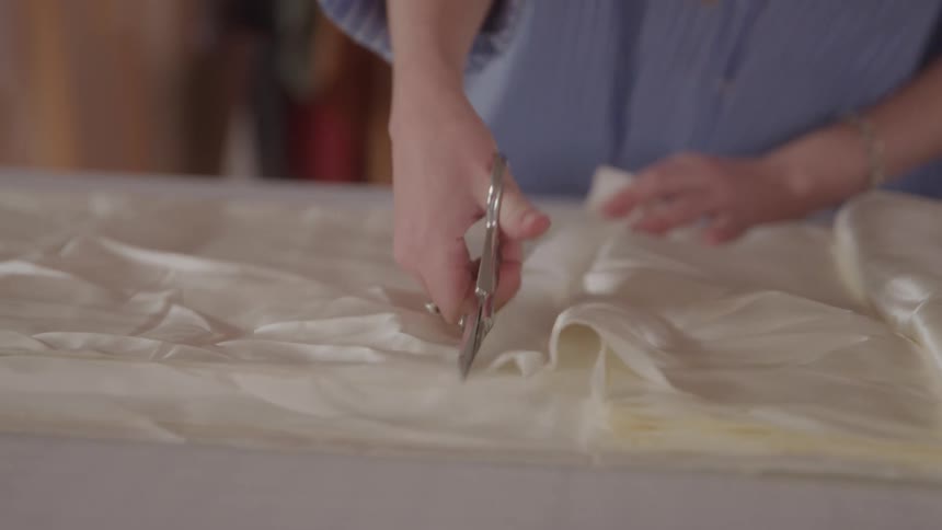A pair of hands skillfully cuts through a sheet of delicate fabric with silver shears