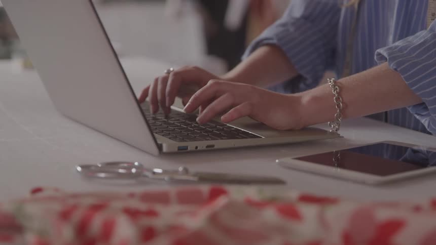 Close up of a female tailor typing on a laptop computer on a table in a room during daytime
