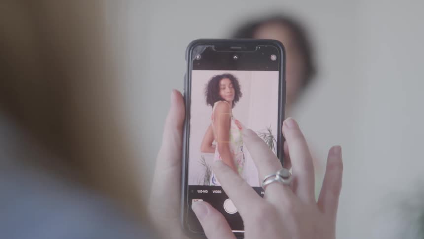 Pair of hands with smartphone taking photos of a woman with curly hair