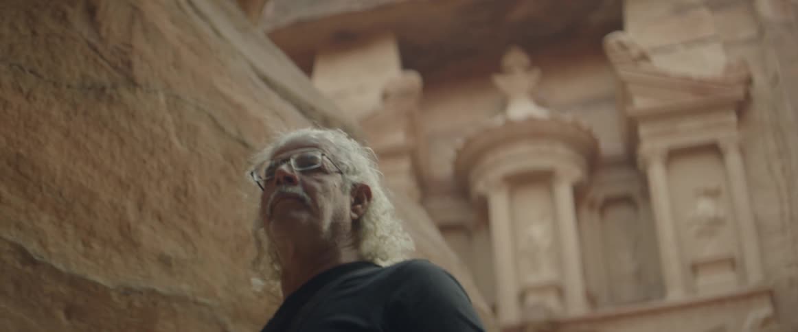 A man walks in a canyon with a building carved in the side