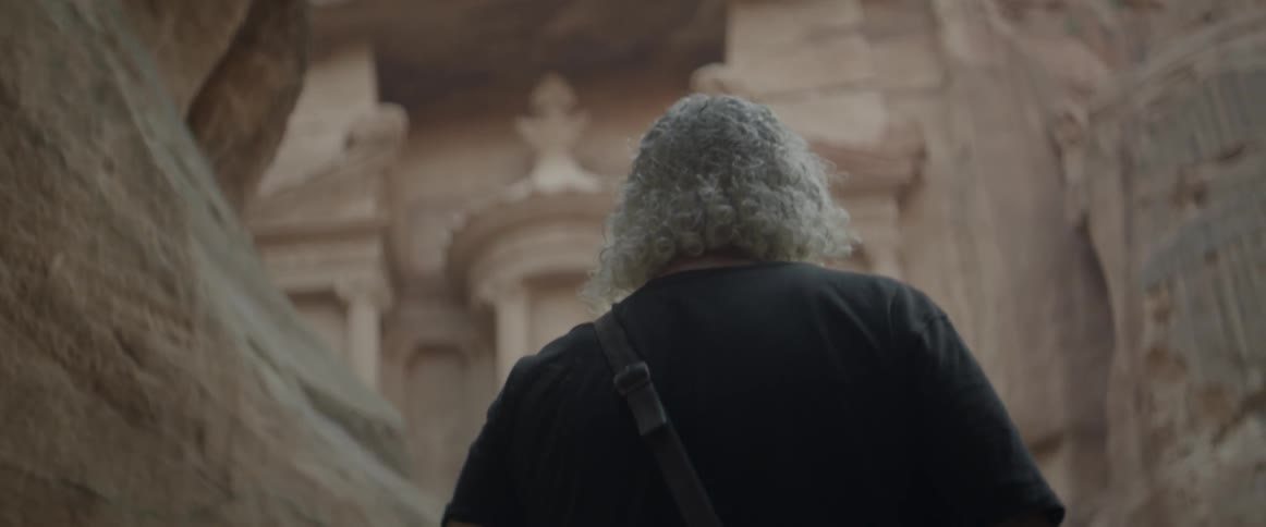 A man approaches a building that is carved into a canyon wall