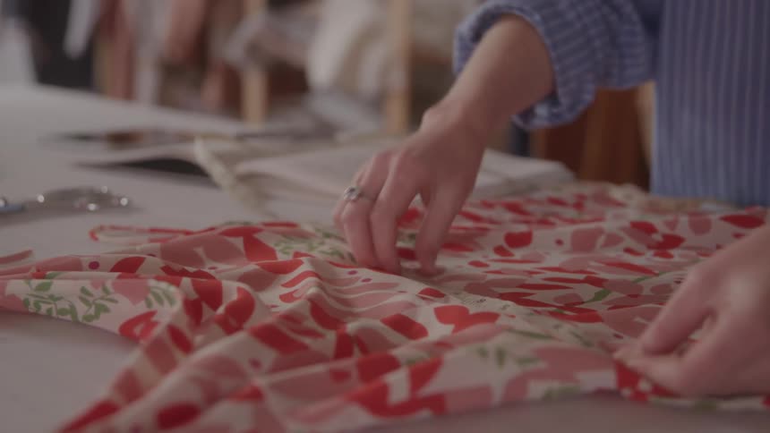 The video shows a persons hands meticulously working with a vibrant floralpatterned fabric likely in a sewing or tailoring context they are seen smoothing the fabric and using a measuring tape suggesting precise garment construction or alteration