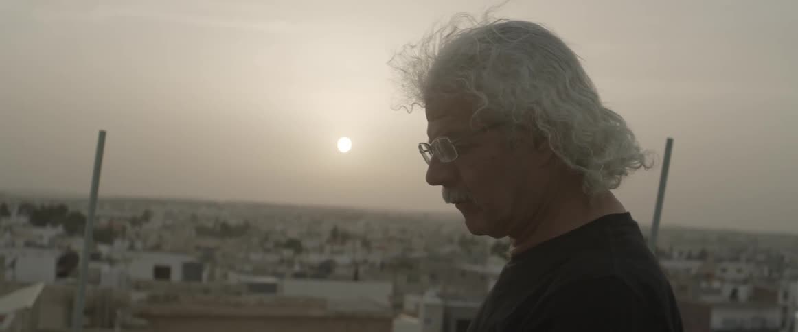 The wind blows a man's hair as he stands outside at dusk