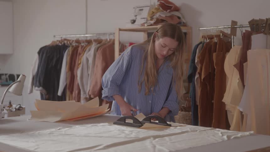 A woman is working with fabric and paper patterns in a clothing studio