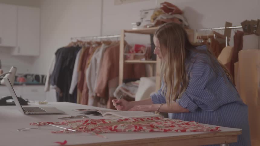 Woman taking notes in a book while in a clothing atelier