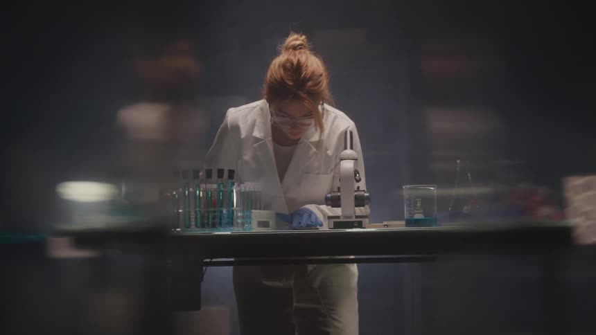 Female scientist examines samples under microscope in dim lab