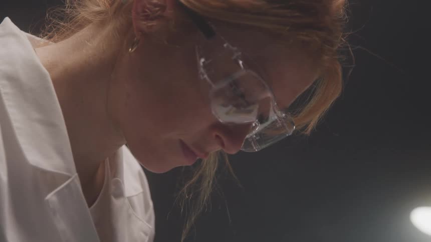 A woman in safety goggles focuses intently on a task