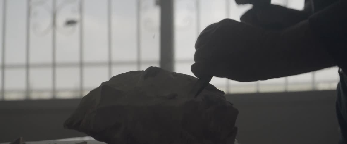 A man uses a chisel and hammer on a rock