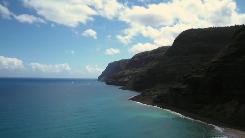 A view of the ocean meeting a mountain and the water is blue and calm