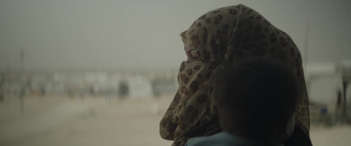 A woman holding a child looks out at the beach