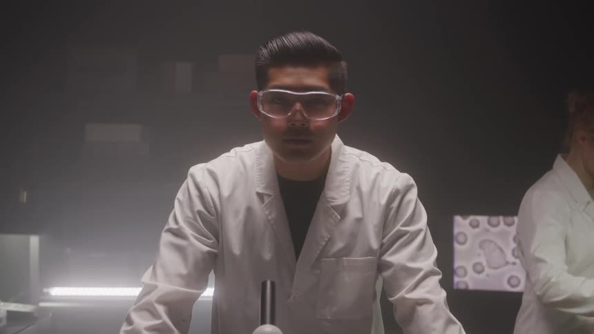 A male scientist in goggles stands at a lab bench with dramatic lighting